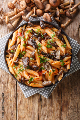 Delicious penne pasta with autumn honey fungus and tomato sauce close-up in a plate. Vertical top view