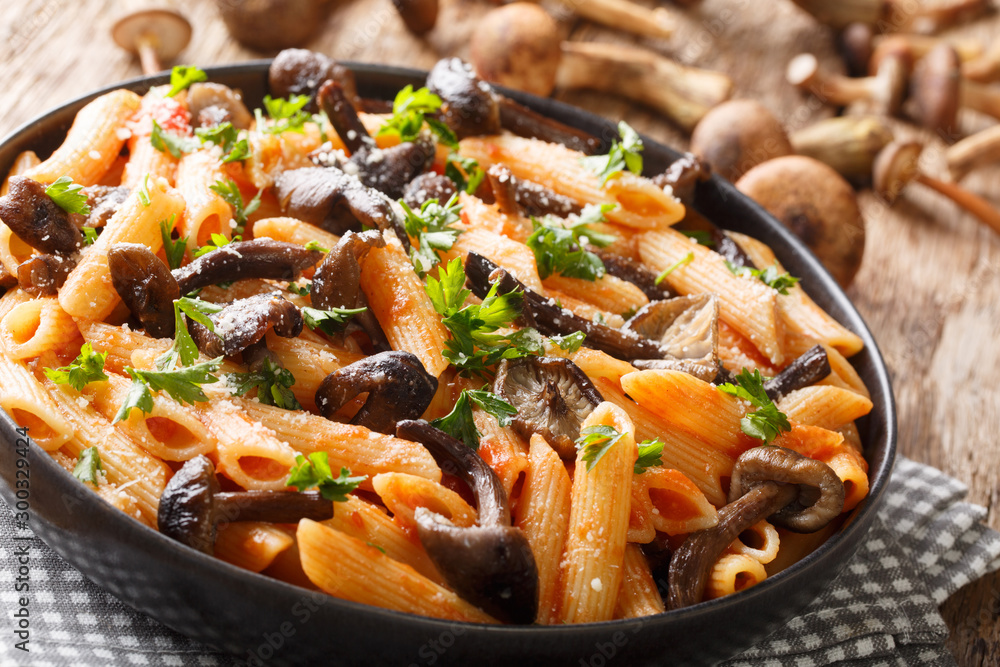 Serving penne pasta with roasted honey mushrooms and tomato sauce close-up in a plate. horizontal Serving penne pasta with roasted honey mushrooms and tomato sauce close-up in a plate. horizontal