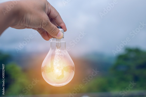 hand holding light bulb against nature, icons energy sources for renewable, 