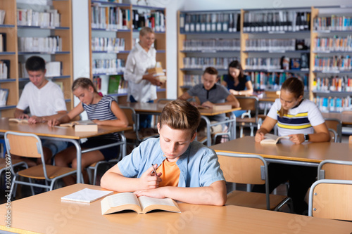 Fotografi Schoolboy preparing for lesson with books in school library indoor
