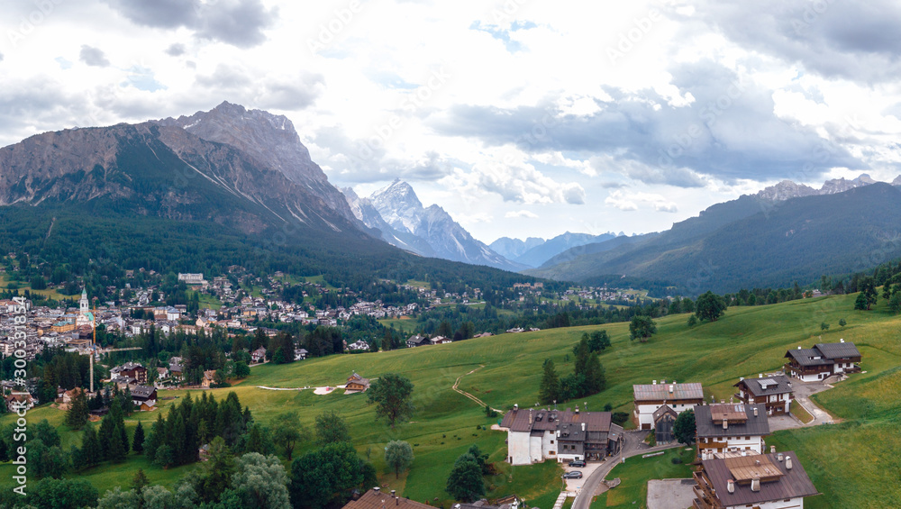 Tourist town Cortina d'Ampezzo, panoramic view with alpine green landscape and massive Dolomites Alps. View of houses and hotels, the city from a height. Province of Belluno, South Tyrol, Italy.