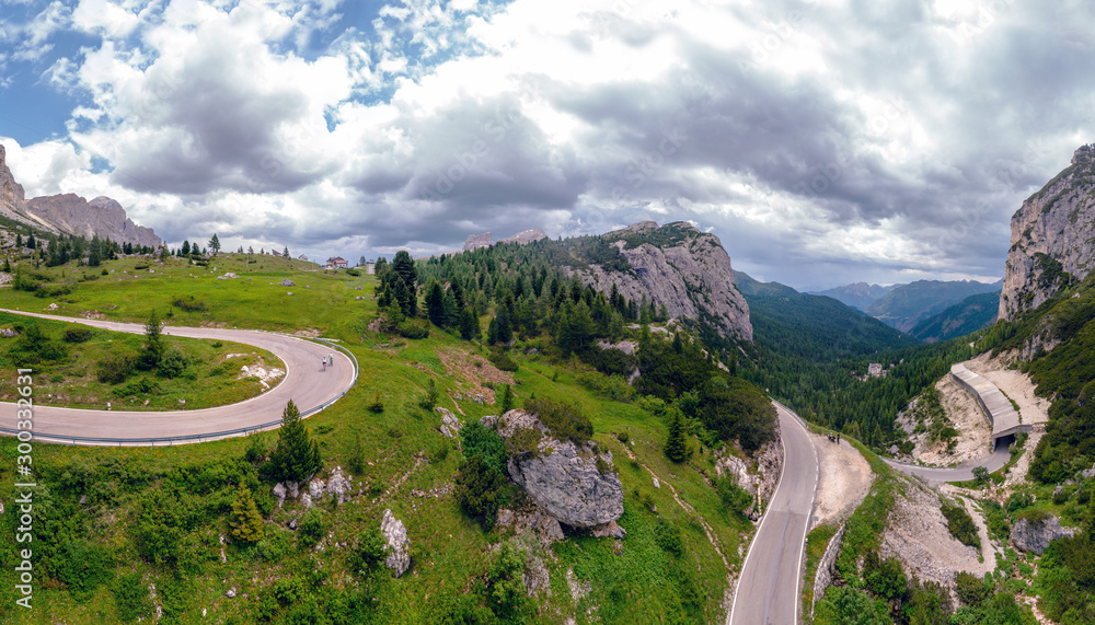 Aerial view of winding road surrounded by mountains, traveling by motorcycle or car, two cyclists riding bicycles on the road, Falzarego Pass, Dolomites, Italy. Cortina d’Ampezzo.