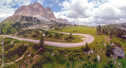 Fototapeta Naklejka Na Ścianę i Meble -  Aerial view of winding road surrounded by mountains, traveling by motorcycle or car, two cyclists riding bicycles on the road, Falzarego Pass, Dolomites, Italy. Cortina d’Ampezzo.