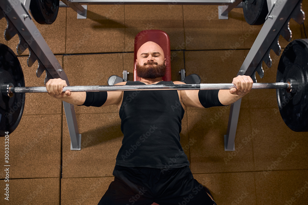 Strong powerful man dressed in black shirt and shorts, having stylish arm  bands, lifting heavy barbell, attempting bench press, looking tired,  expressing strength, top view Stock Photo | Adobe Stock