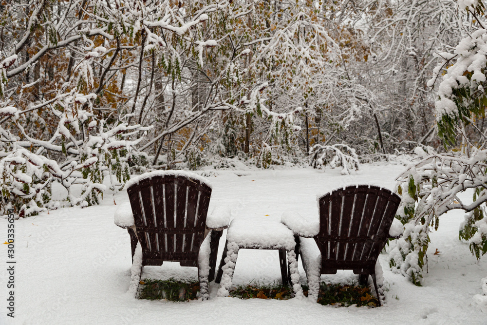 Unexpected snowfall in October covers lawn furniture with white fluffy snow.