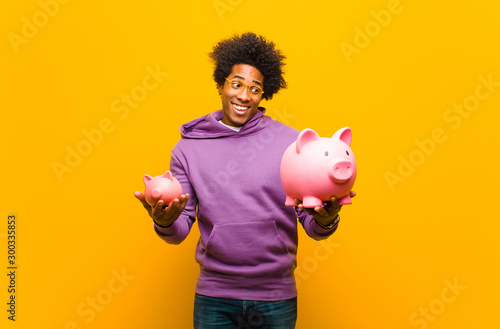 young african american man with a piggy bank against orange back photo