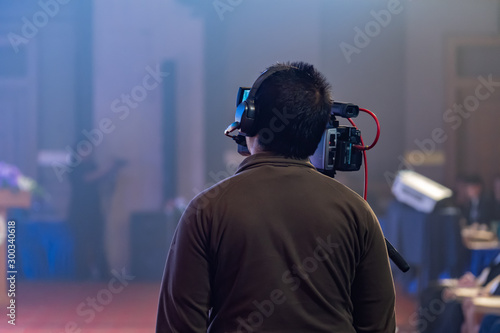 Tv OB camera in a concert or conference hall.Video cameras operator working with his equipment, Cameraman in a meeting room, light Bokeh in Background, selective focus.Vintage filtered photo process.