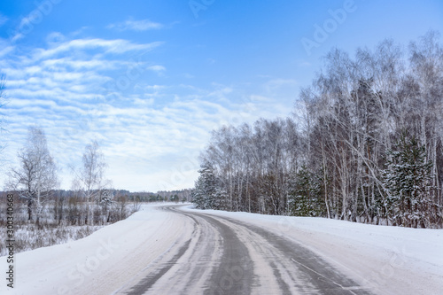 Patterns on the winter highway in the form of four straight lines. Snowy road on the background of snow-covered forest. Winter landscape.