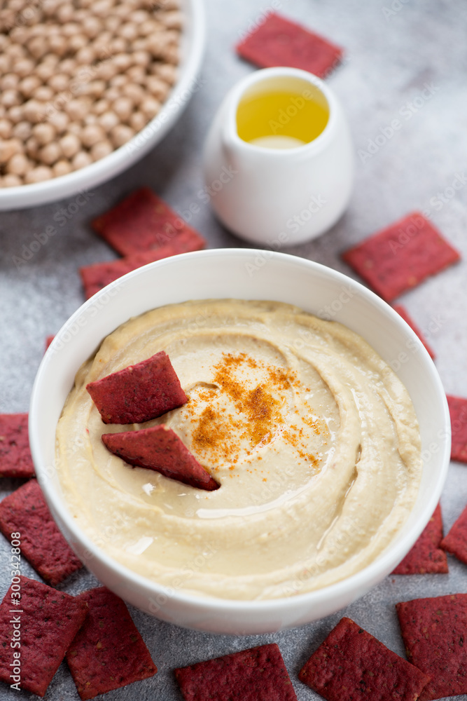 White bowl with hummus and beetroot crackers, studio shot on a beige stone background