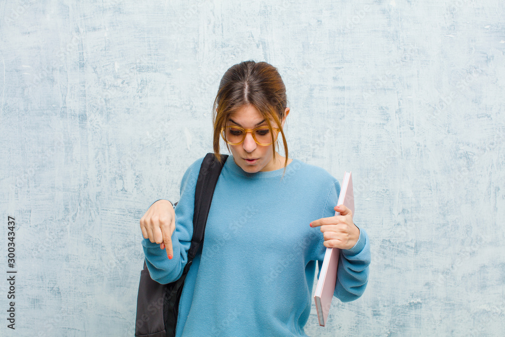 Φωτογραφία young student woman feeling shocked, open-mouthed and amazed, looking and pointi