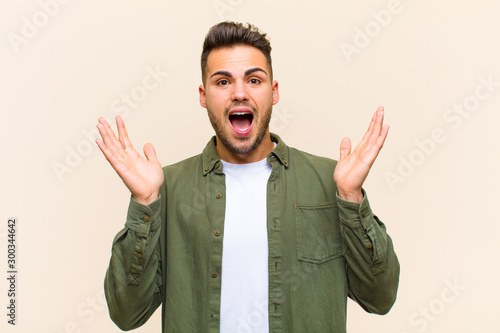 young hispanic man feeling happy, excited, surprised or shocked, smiling and astonished at something unbelievable against isolated background photo