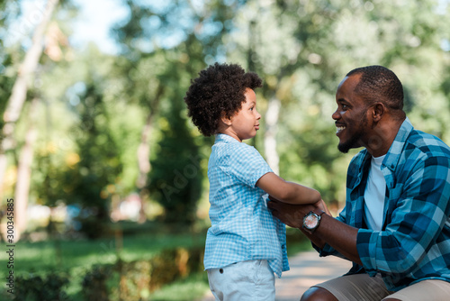 side view of cheerful african american father holding hands with son