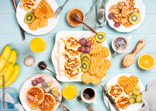 Flat lay with healthy breakfast with fresh hot waffles hearts, pancakes flowers with berry jam and fruits on turquoise background, top view, flat lay. Food concept. © Iryna Melnyk