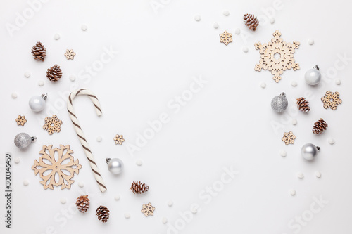 Christmas border made of wooden snowflakes, christmas ornaments, pine cones and white pompons. White background. Flat lay, top view.