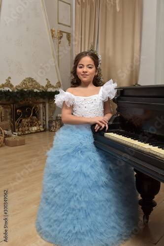 girl young princess in white with a blue dress and a barrette in black hair curls at the piano