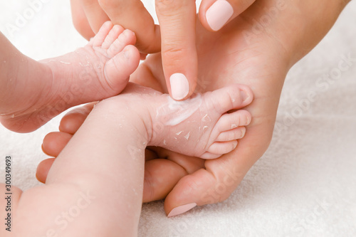 Female hand holding newborn leg. Mother carefully applying medical ointment on dry skin. First days after birth. Care about baby clean and soft body skin. Close up.