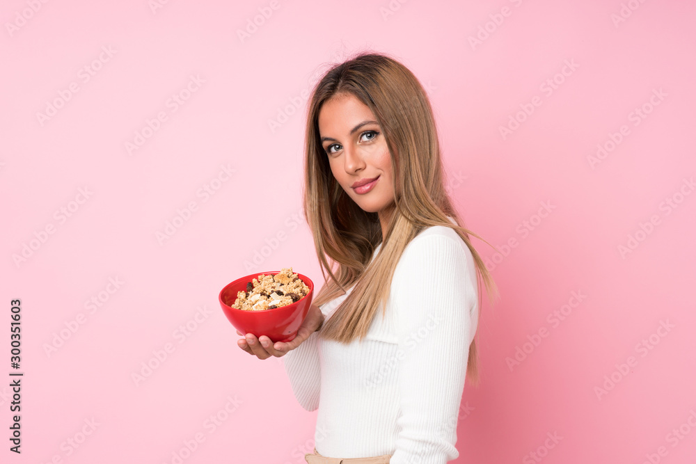 Young blonde woman over isolated pink background holding a bowl of cereals Young blonde woman over isolated pink background holding a bowl of cereals