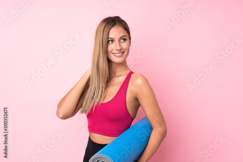 Young sport blonde woman over isolated pink background with a mat © luismolinero
