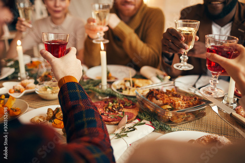 Close up of modern adult people raising glasses while enjoying Christmas dinner at home, copy space