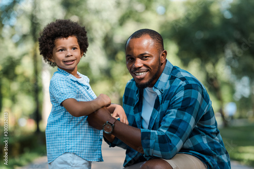 cute curly african american kid holding hands with cheerful father © LIGHTFIELD STUDIOS