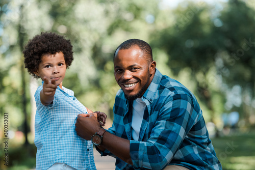 happy african american man looking at camera near cute son pointing with finger © LIGHTFIELD STUDIOS