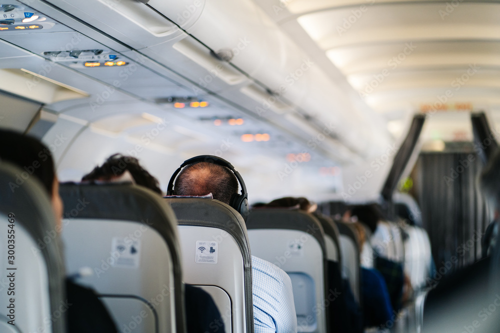 man listens to music in headphones on a plane - obrazy, fototapety, plakaty 