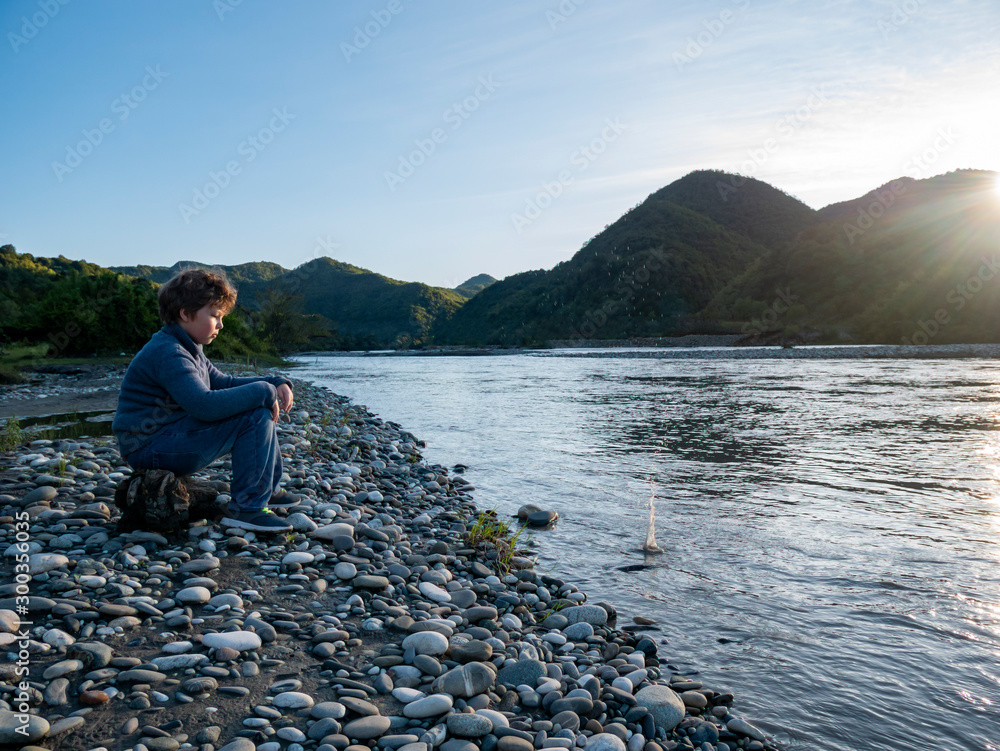 The child studies the stoun on mountain river beach The child studies the stoun on mountain river beach