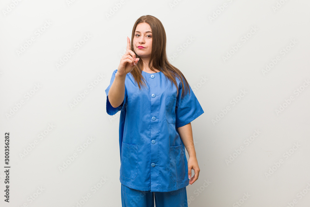 Young nurse woman against a white wall showing number one with finger. Young nurse woman against a white wall showing number one with finger.