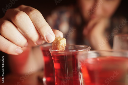 a young male teenager puts yellow sugar in a Cup of tea, holding it in his hands over a glass