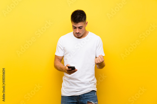 Young handsome man over isolated yellow background surprised and sending a message