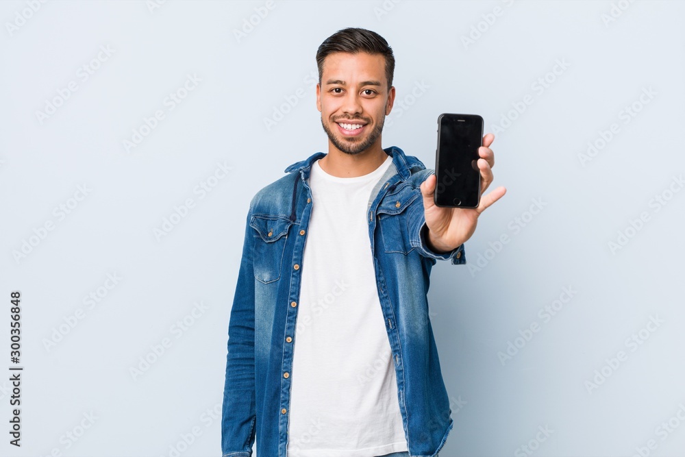 Young south-asian man holding a phone - obrazy, fototapety, plakaty 