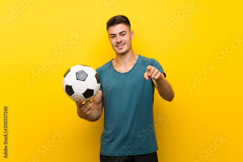 Handsome young football player man over isolated yellow background points finger at you with a confident expression