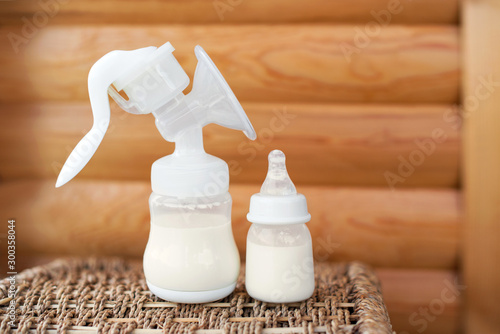 Breast pump and bottle with breast milk for baby on wooden background. Maternity and baby care concept. Top view.