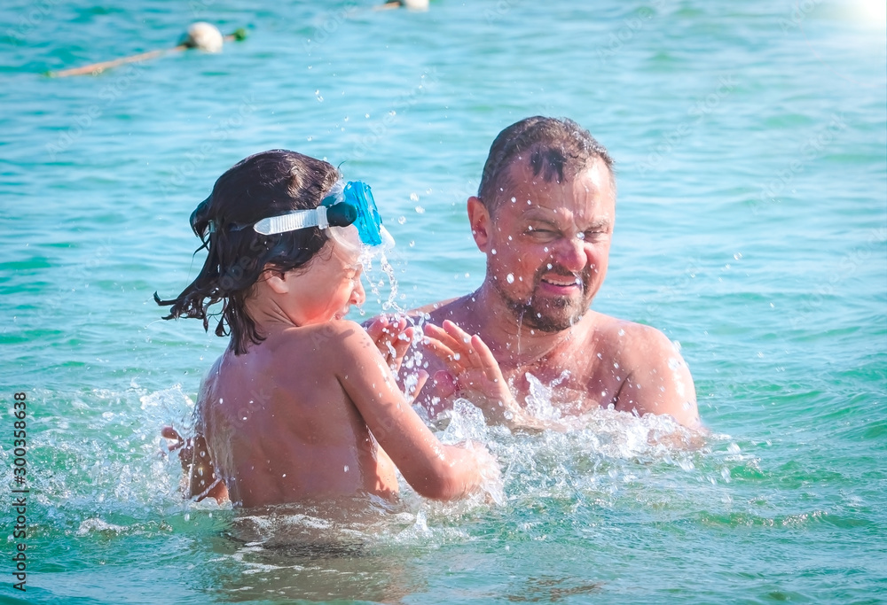 Father and son are playing inside the sea. Summer holiday concept.