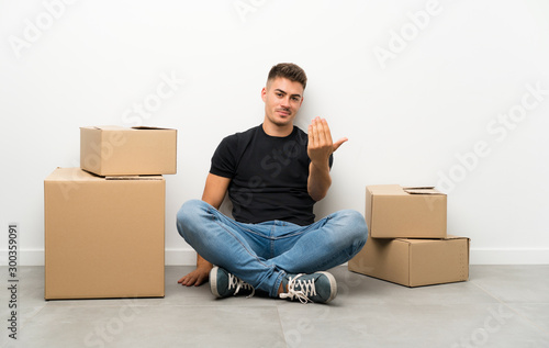 Handsome young man moving in new home among boxes inviting to come