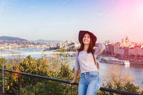 A happy young woman enjoying her trip to Budapest, Hungary from the point from Gellert Hill during sunrise in autumn during sunrise.