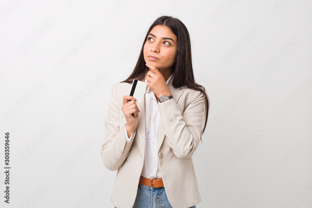 Young arab woman holding a credit card looking sideways with doubtful and skeptical expression. Young arab woman holding a credit card looking sideways with doubtful and skeptical expression.