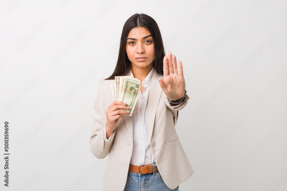 Young arab business woman holding dollars standing with outstretched hand showing stop sign, preventing you. Young arab business woman holding dollars standing with outstretched hand showing stop sign, preventing you.