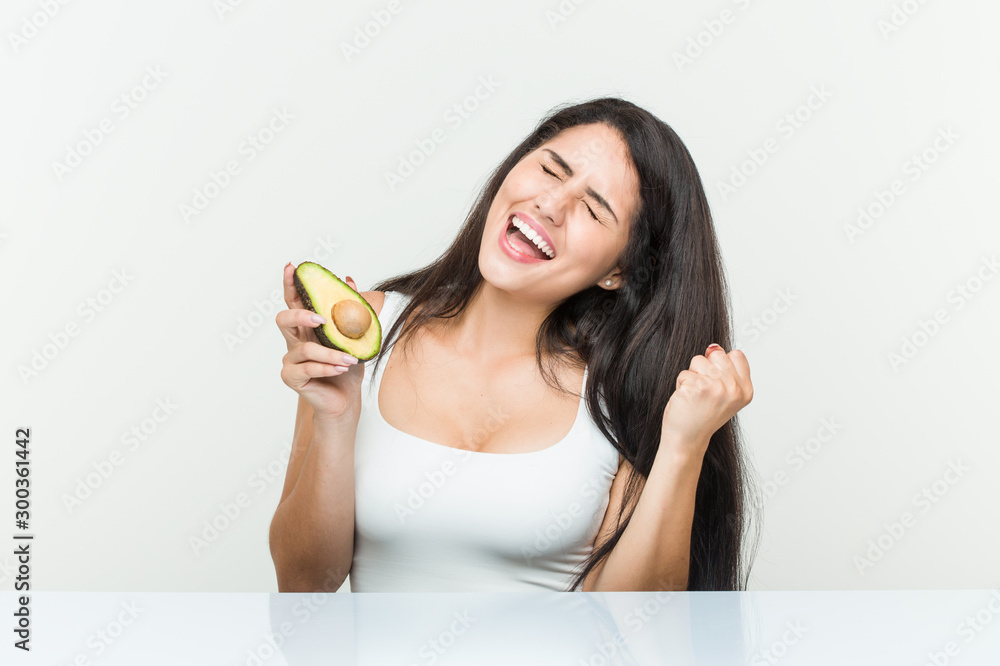 Young hispanic woman holding an avocado cheering carefree and excited. Victory concept. Young hispanic woman holding an avocado cheering carefree and excited. Victory concept.