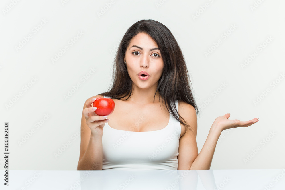 Young hispanic woman holding a tomato impressed holding copy space on palm. Young hispanic woman holding a tomato impressed holding copy space on palm.