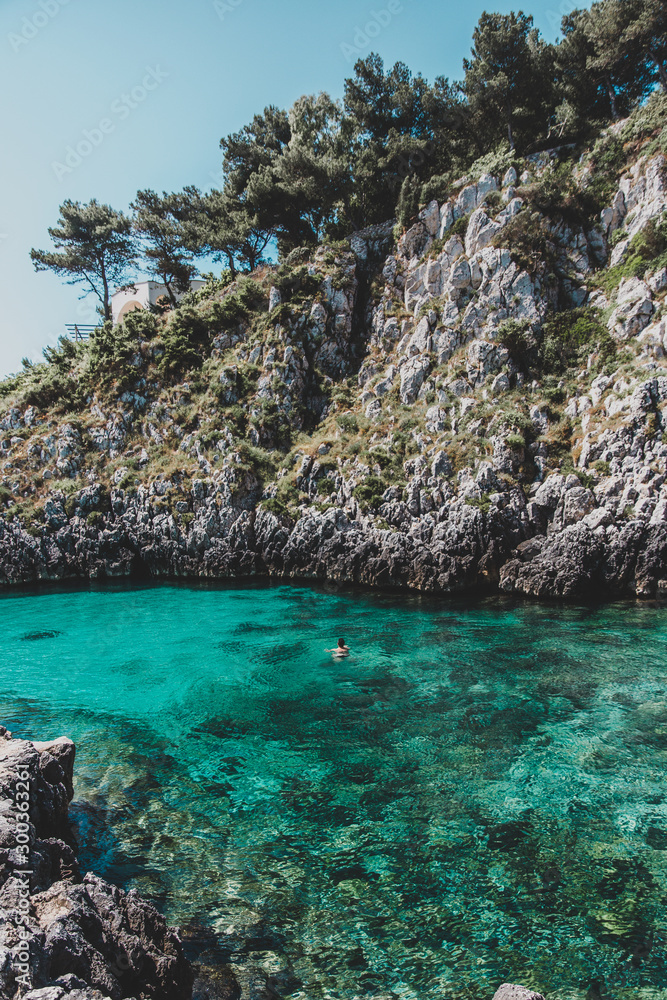 person swimming alone in crystal clear water in Cala Dell'Acquaviva in Puglia, Italy
