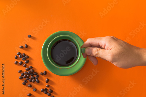 Taking green cup of coffee with coffee beans on orange background
