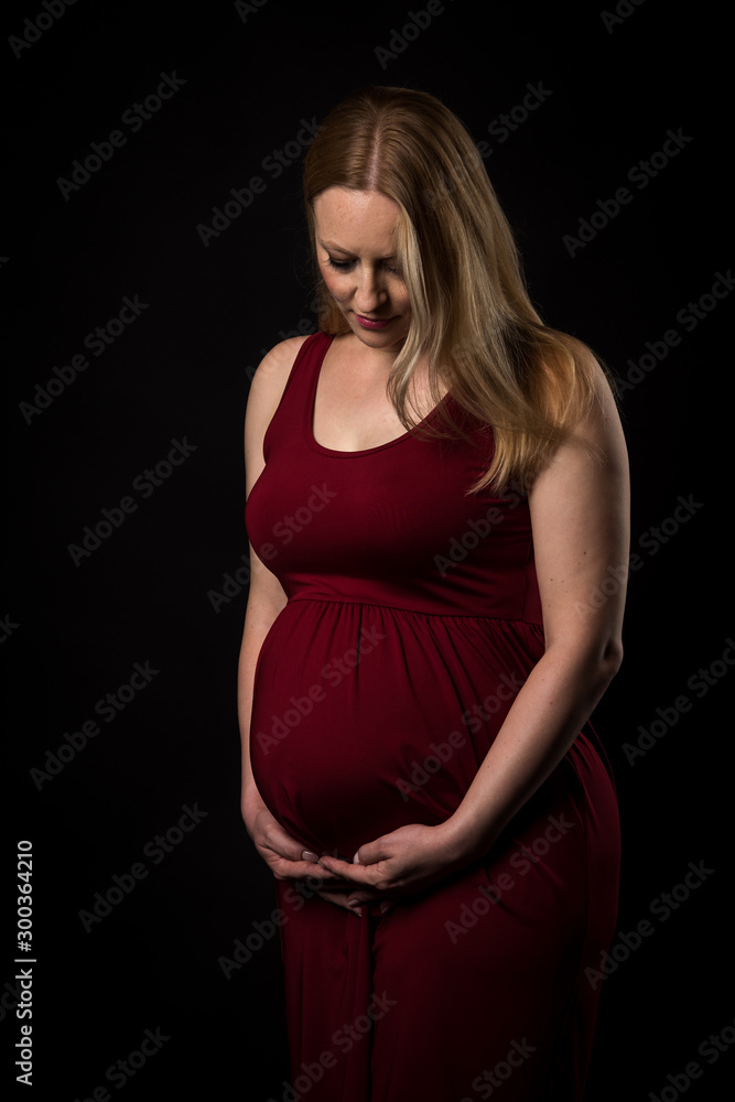 Pregnant woman in red dress holding belly on black background. Pregnant woman in red dress holding belly on black background.