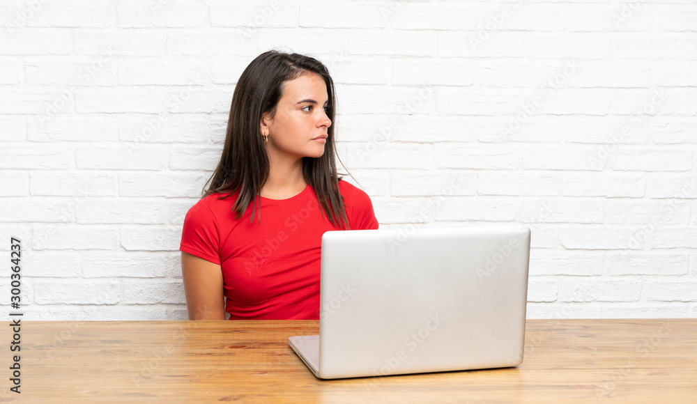 Young girl with pc in a table looking side Young girl with pc in a table looking side