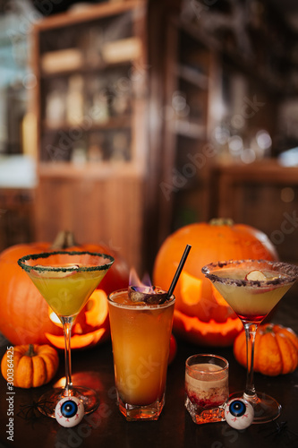 A close up shot of Halloween cocktails with carved pumpkins in the background. Concept of seasonal traditions and celebration in hospitality. Selective focus on the cocktails. © Olga