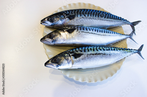 Three mackerels on a white plate lie on the table