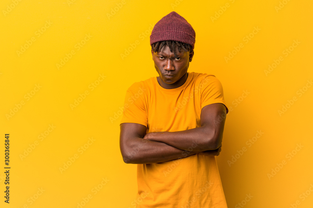 Young black man wearing rastas over yellow background frowning face in displeasure, keeps arms folded. Young black man wearing rastas over yellow background frowning face in displeasure, keeps arms folded.