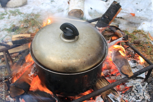 The pan stands on a fire and burning coals, against a background of white snow