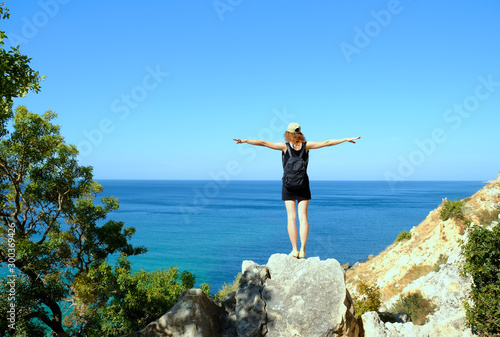 Girl doing airplane with arms outstretched. Young woman standing on a rock and looking at the sea. Freedom and healthy lifestyle concept. 