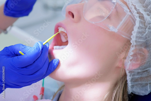 Dentist make fluoridation of teeth after ultrasonic cleaning for young woman. Stomatologist apply fluoride on patient's teeth. Portrait of young woman. Stomatology clinic, cure, treatment, procedure. photo
